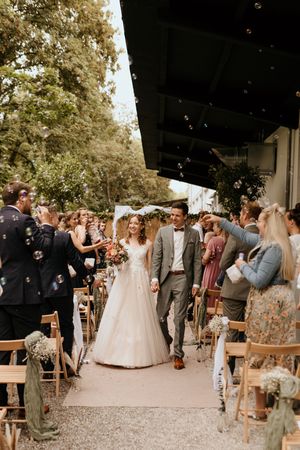 Outdoor wedding ceremony setup with wooden chairs and guests gathering under trees.