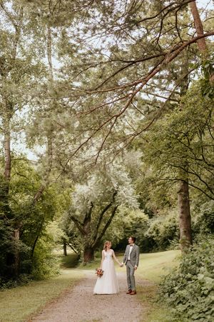Couple walking along a tree-lined path in wedding attire during golden hour.