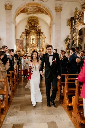Elegant church ceremony with guests gathered in ornate baroque interior with gilded details and wooden pews.