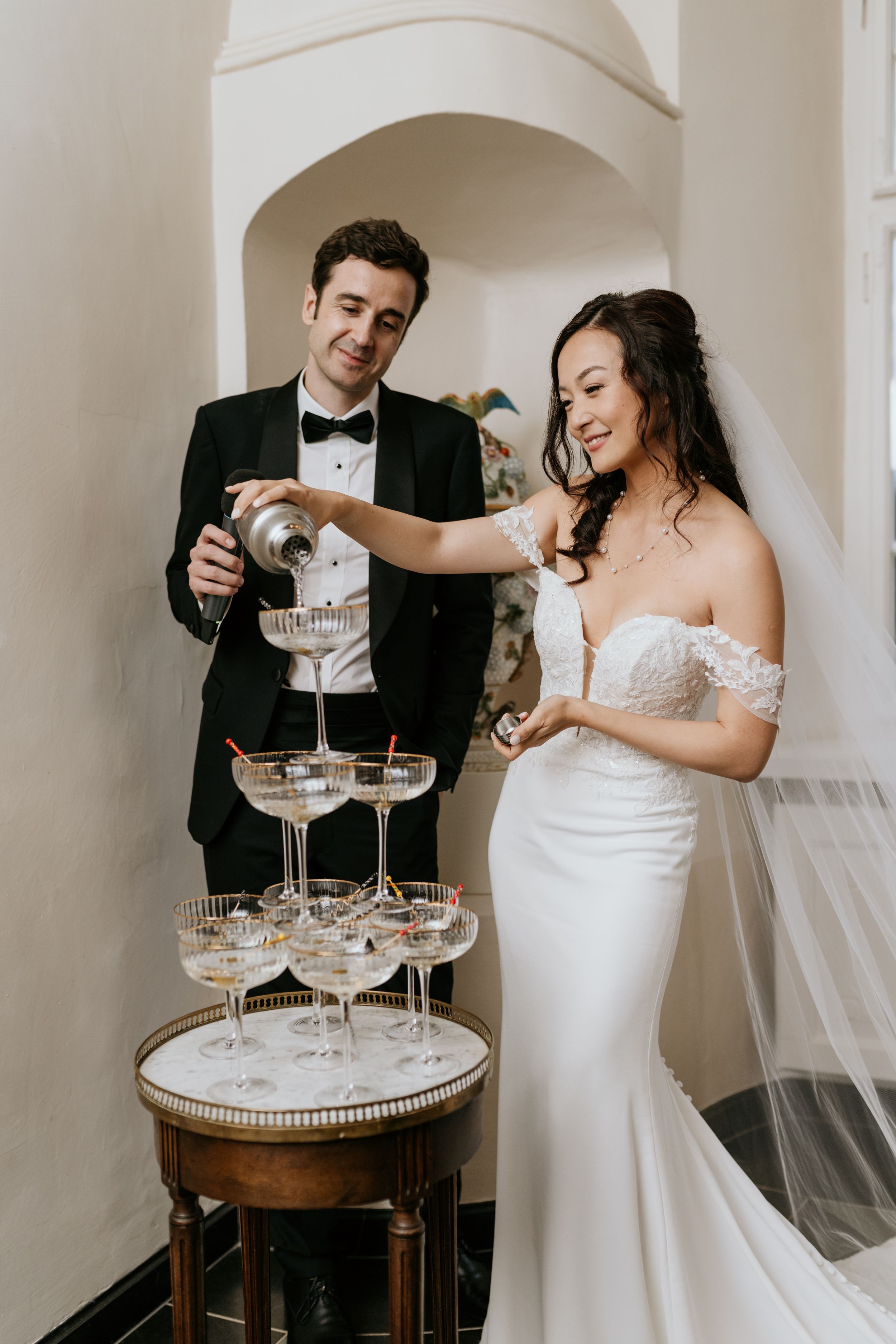 Couple pouring champagne into a tower of elegant crystal glasses at a wedding celebration.