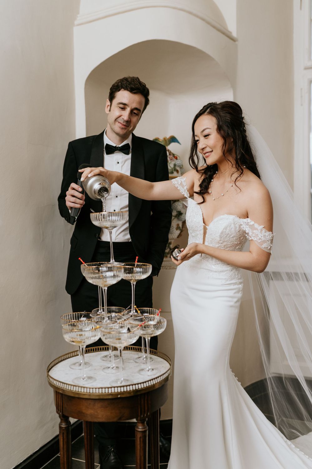Couple pouring champagne into a tower of elegant crystal glasses at a wedding celebration.
