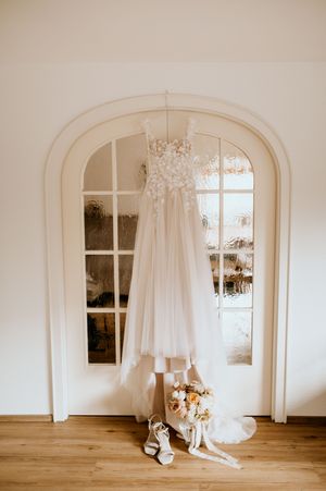White wedding dress and accessories displayed in elegant room with arched windows.