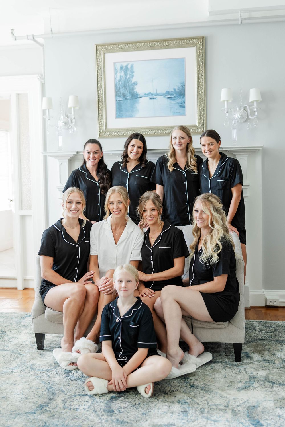 Group wearing matching black sleepwear sits together on floor in elegant white room with framed artwork.