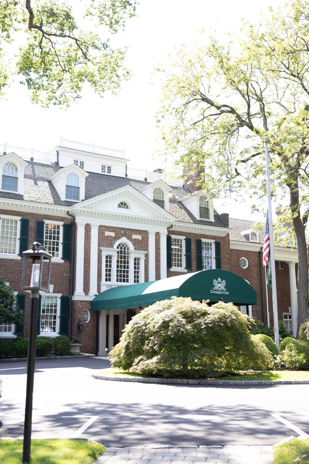 Elegant colonial-style brick building exterior with white columns and black shutters surrounded by manicured landscaping.