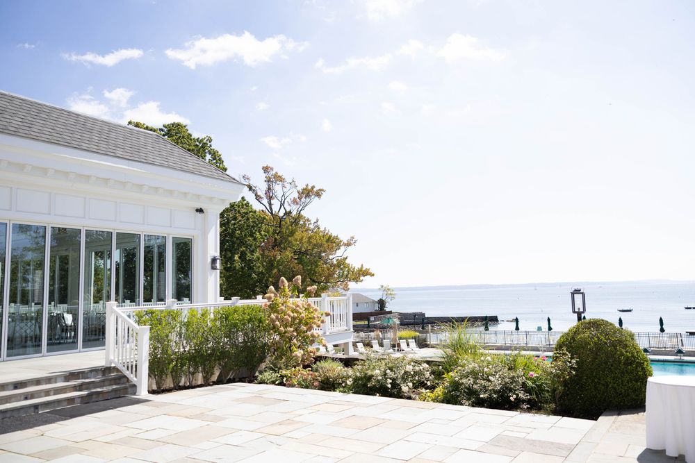Panoramic view of a modern white building exterior with glass windows and walkways against a bright blue sky.
