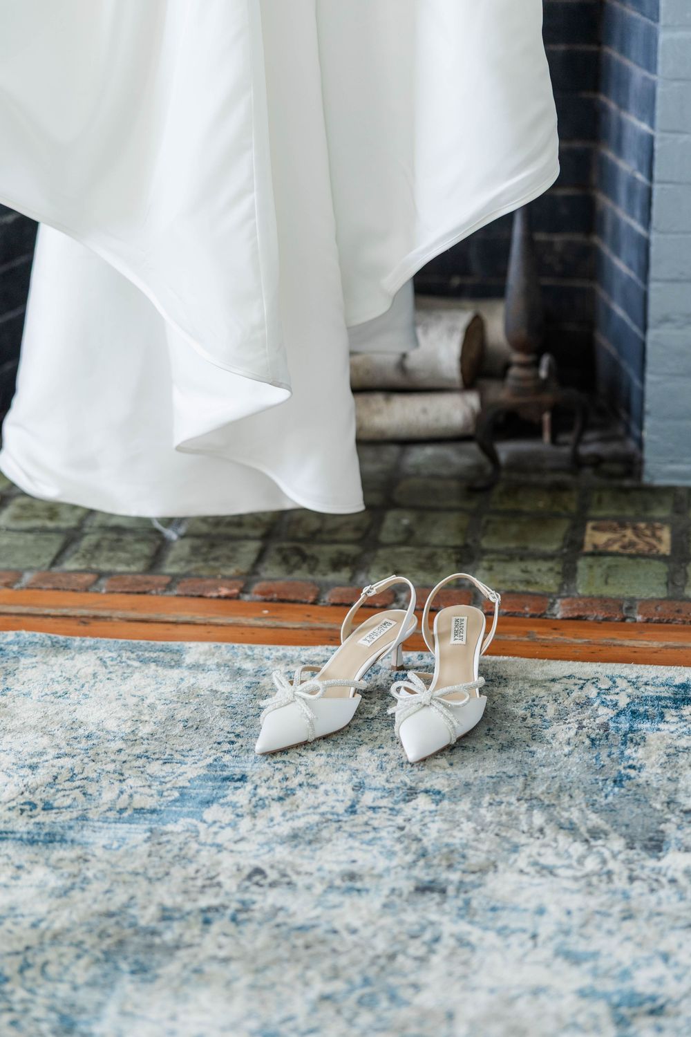 Close-up of white bridal shoes on a blue vintage rug against hardwood flooring.