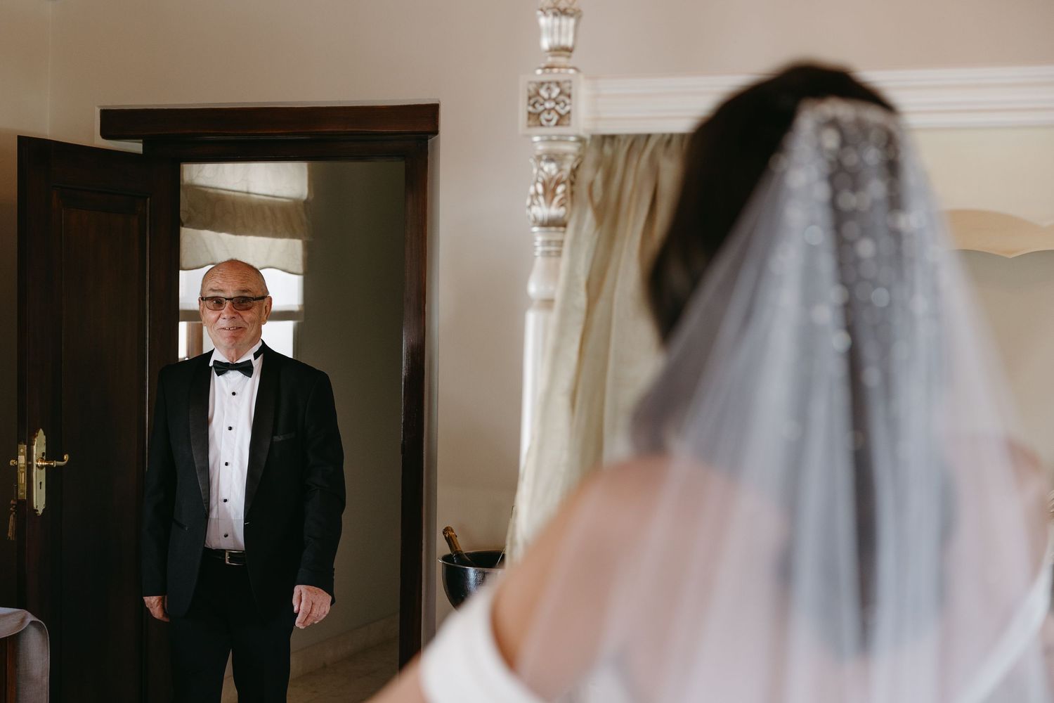 A wedding party stands in a formal hallway with elegant white decor and dark wooden doors.