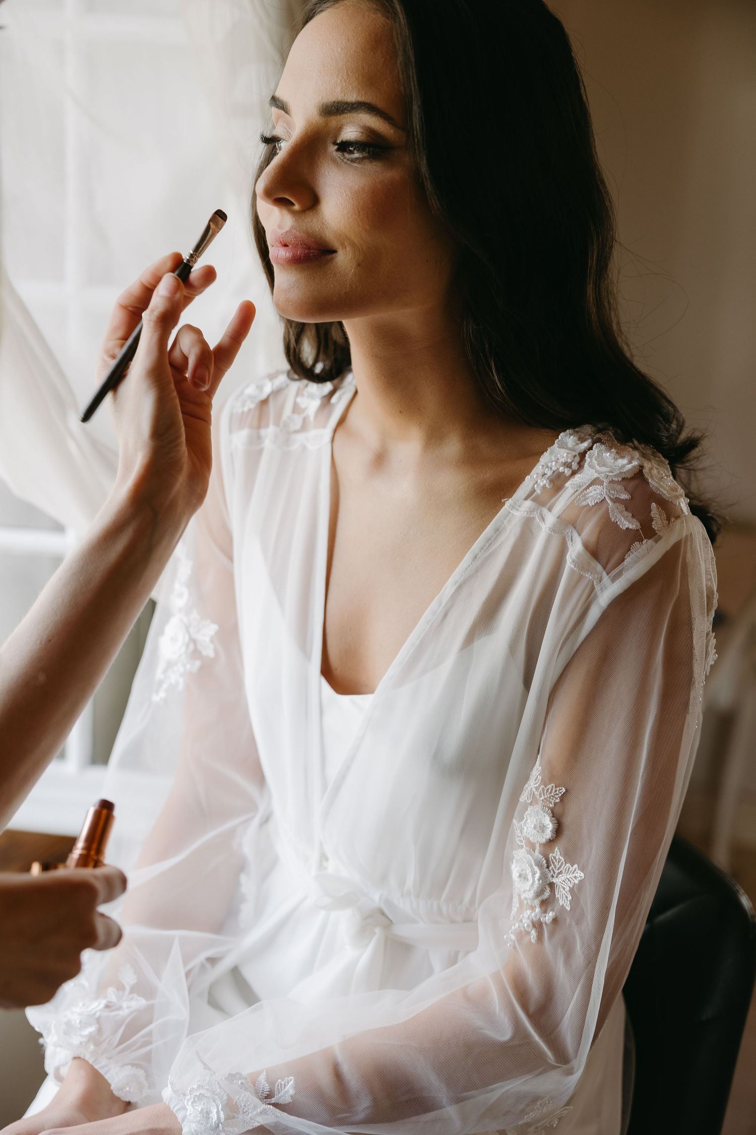 A series of photos showing someone in a delicate white lace robe getting their makeup done during preparation.