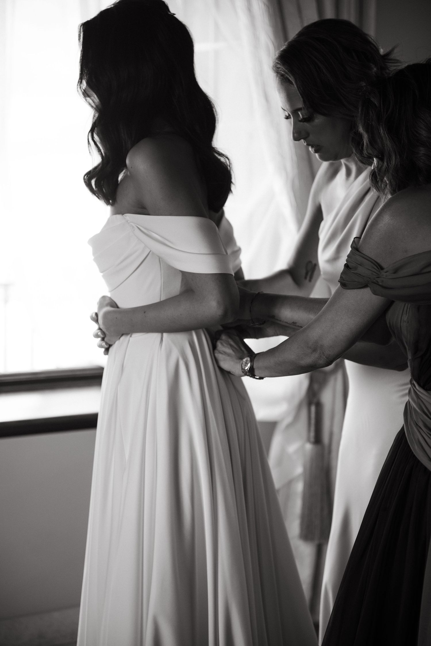 Black and white photo series showing the back of a flowing white wedding dress being fastened or adjusted.