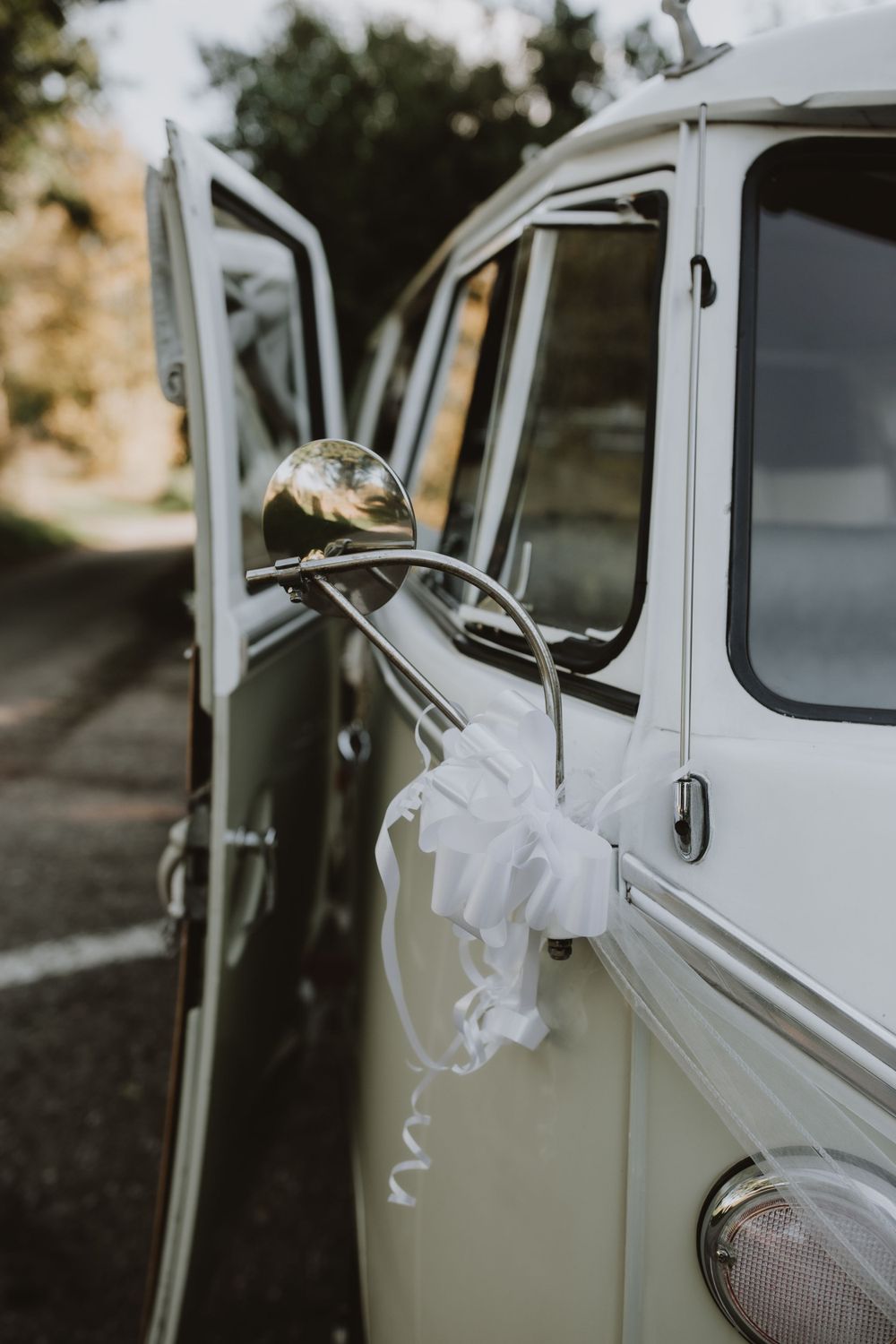 A classic white vintage car with open door decorated with flowing white ribbons for a wedding celebration.