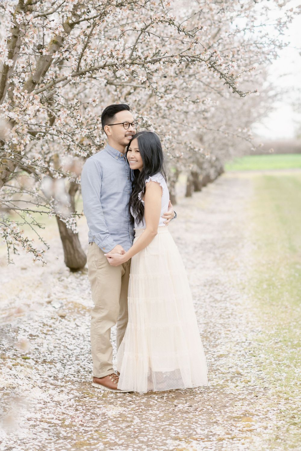 A couple embraces under cherry blossom trees during a spring photo session.