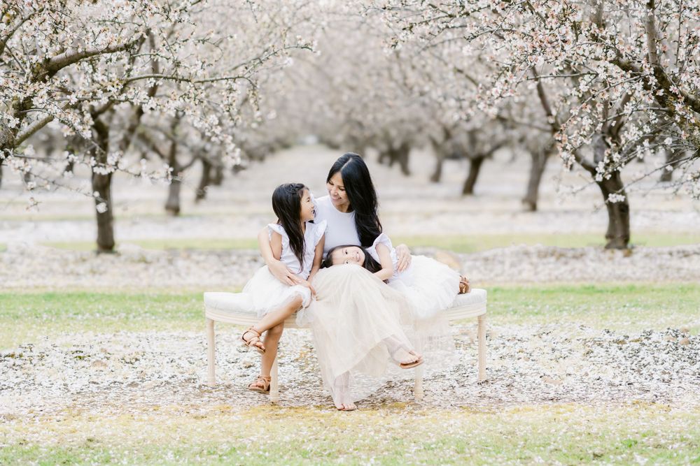 Two friends in white dresses twirling together under cherry blossoms in an orchard.