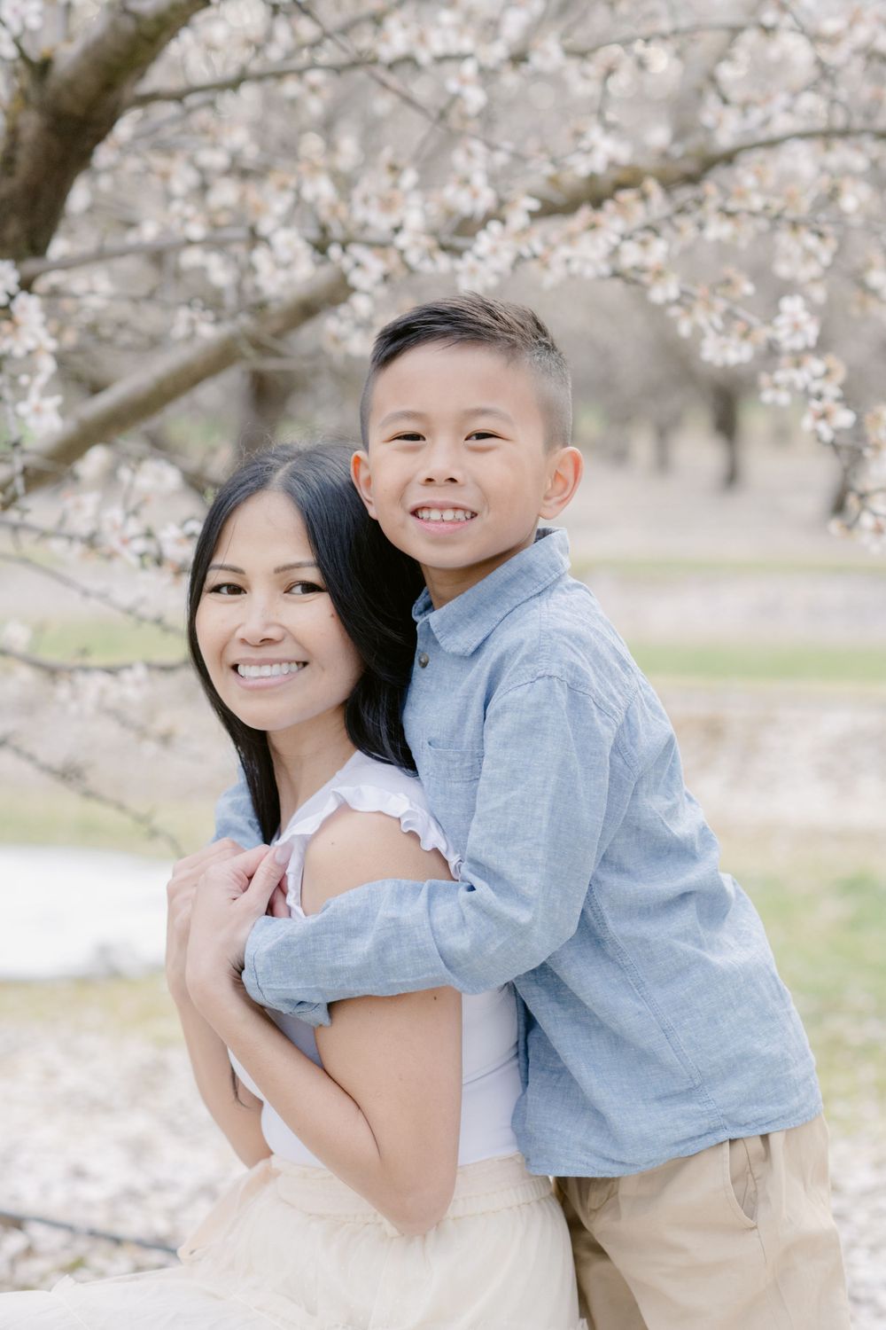 A joyful embrace between parent and child under flowering cherry blossom trees.