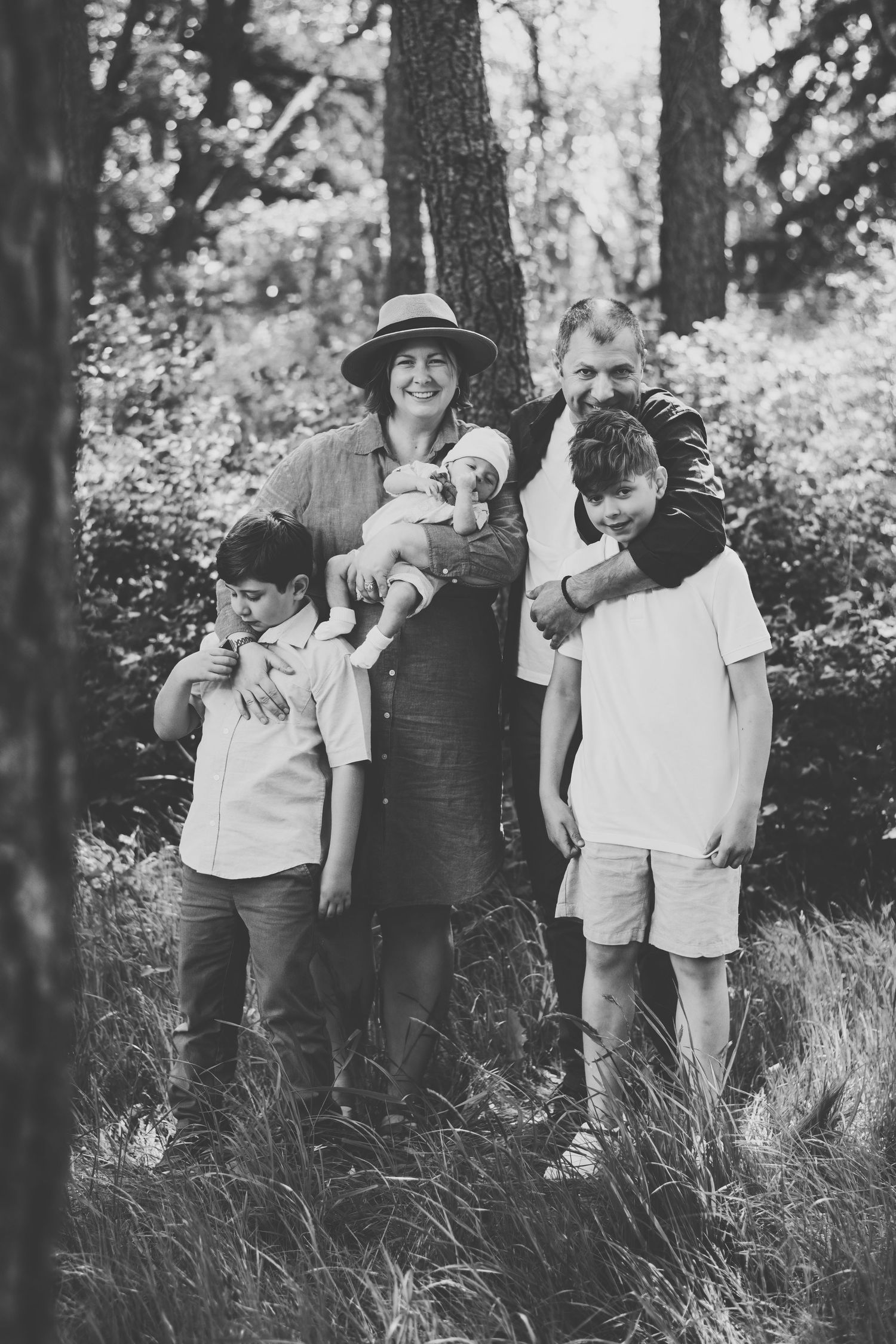 Black and white portrait of a family gathered together in a natural outdoor wooded setting.