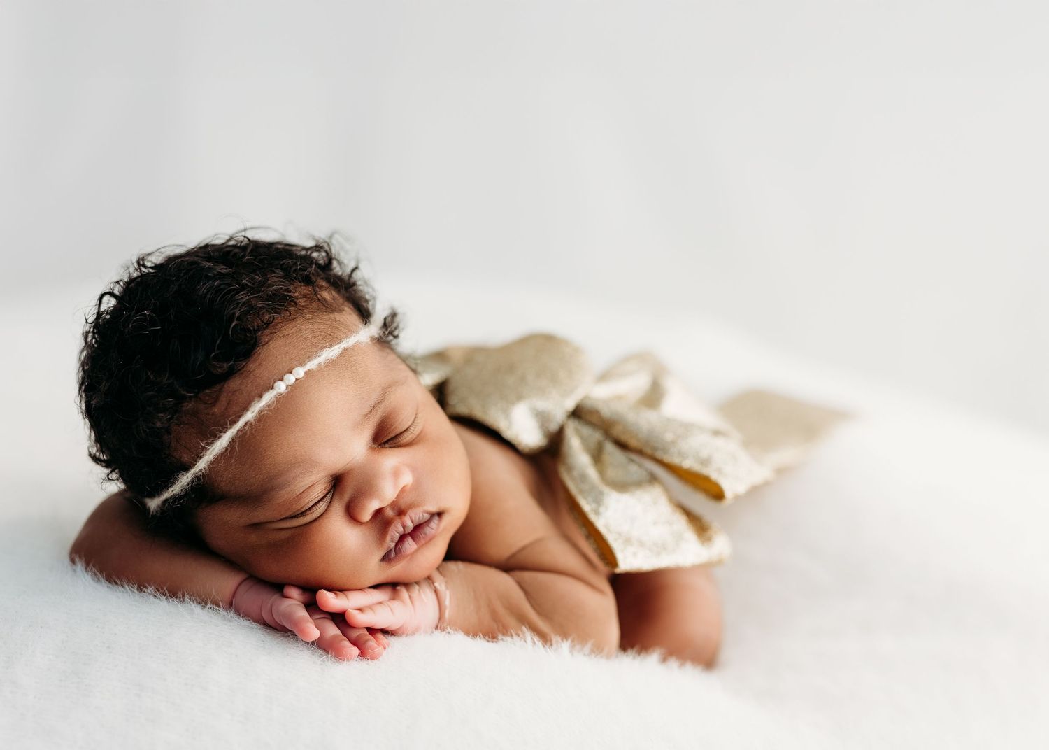 Sleeping newborn baby wearing white headband rests peacefully on white blanket with hands under cheek. Rashinphotography - Nova photographer