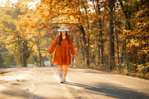 Person in orange dress walking down autumn path surrounded by golden trees.