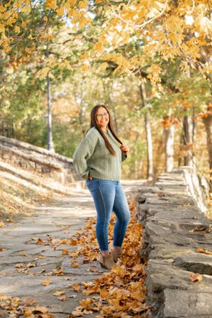 Autumn outdoor portrait on stone steps with yellow leaves and trees in background.