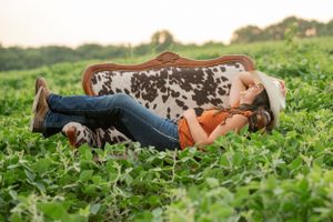 Person in western attire lying on spotted cowhide in green field.