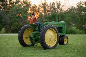 Classic John Deere Model A tractor parked on grass during sunset.