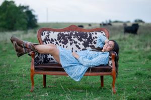 Someone relaxing on a vintage cowhide-upholstered bench outdoors in a country setting.