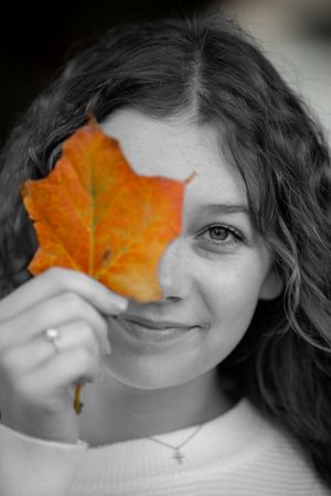 A selective color photo showing an orange autumn leaf held up against a black and white portrait.