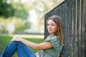Relaxed portrait sitting against black fence in natural outdoor setting.