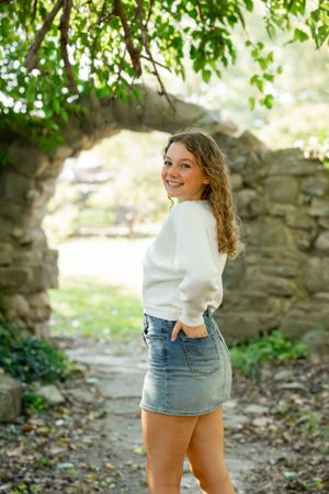 Person in white sweater posing under stone archway in garden setting.