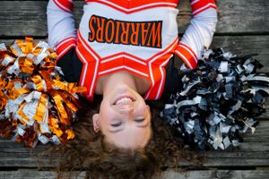An overhead shot of a cheerleader laying on wooden planks with orange and black pom poms.