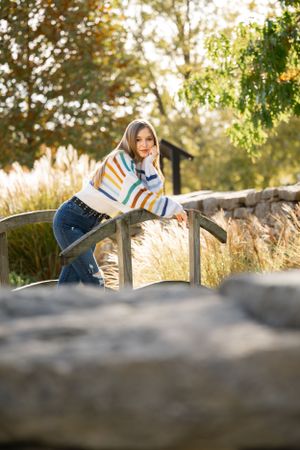 Person in striped sweater leaning on wooden railing surrounded by autumn foliage.