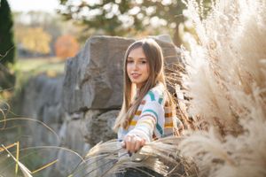 Person in striped sweater poses near rocky wall with sunlit grasses in background.