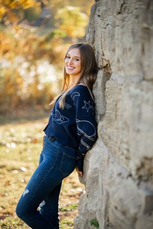 Person in navy space-themed sweater leaning against stone wall in autumn setting.