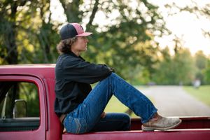 Person in casual attire sitting on red truck bed at sunset.