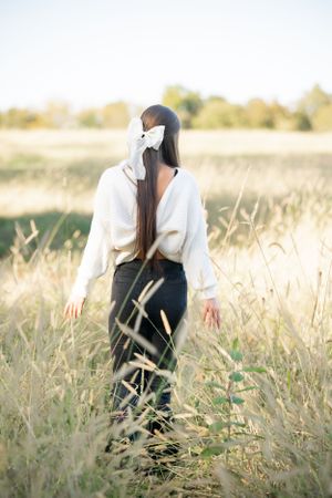 Figure stands in a golden field of tall grass at sunset wearing a white top and dark pants.