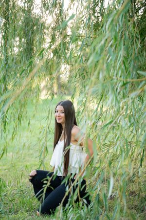 Person sits among graceful willow branches in a serene garden setting.