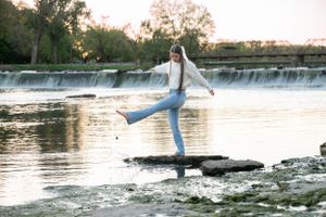 Figure in flowing outfit balances on rock near cascading waterfall at sunset.