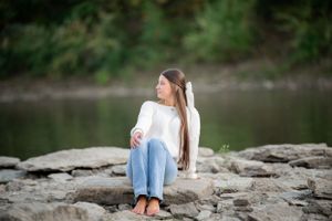 Person in casual attire sits peacefully on rocky riverbank overlook.