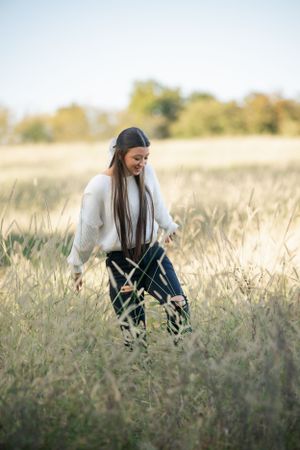 A person in a white sweater explores a tall grass field on a sunny day.