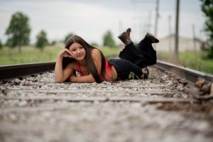A person lies on railroad tracks during a casual photoshoot in casual attire.