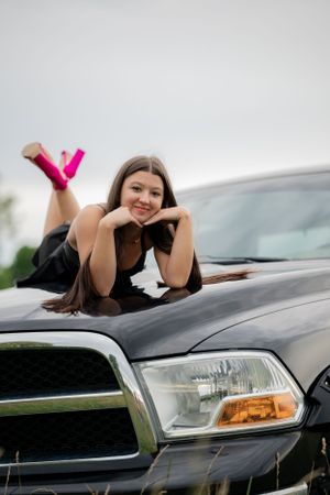 A person lies on the hood of a black Dodge Ram truck wearing pink shoes.
