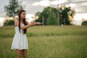 A person in a white summer dress stands in a golden field at sunset.