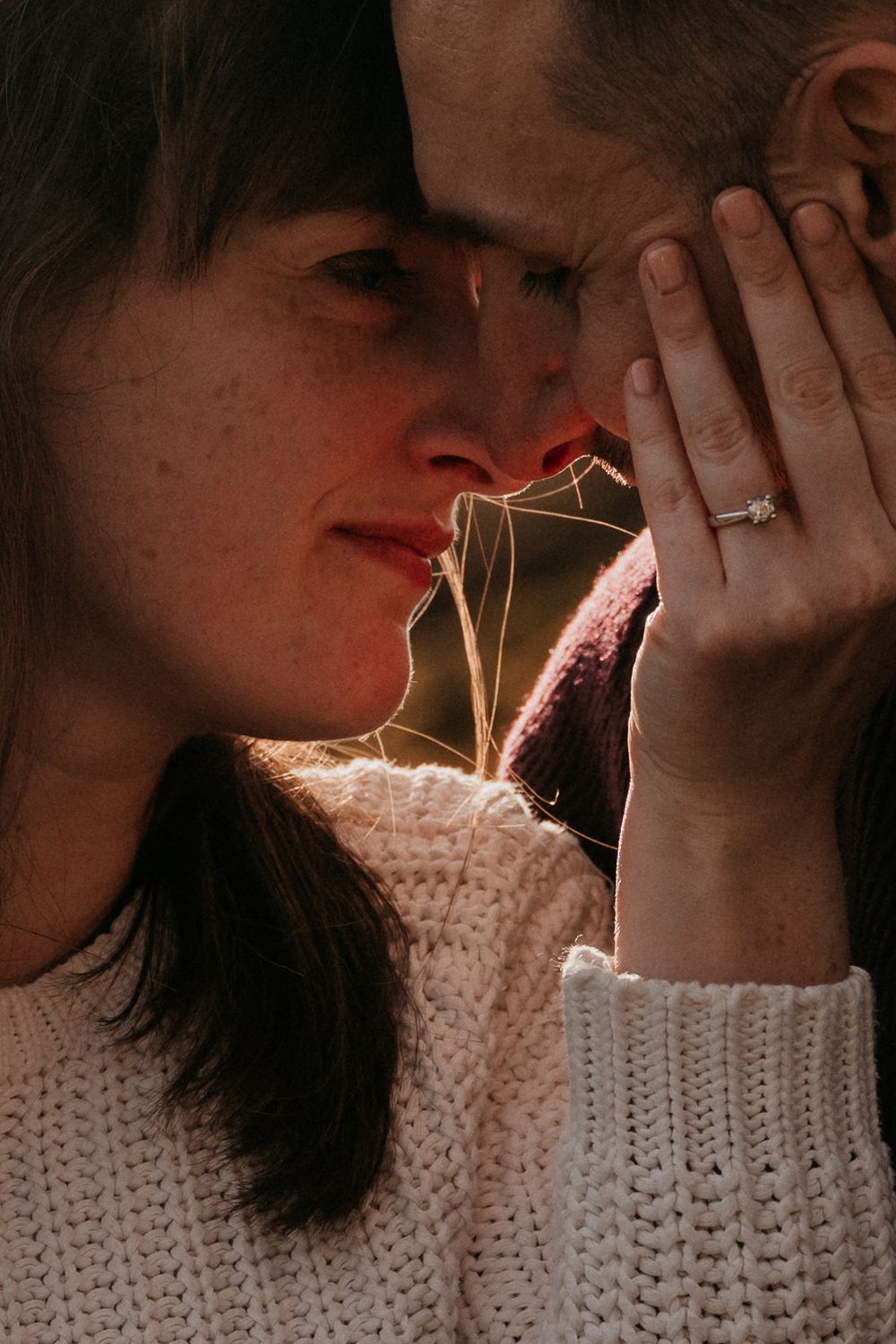 Close-up of a couple sharing an intimate moment, woman displaying a diamond engagement ring on her finger.