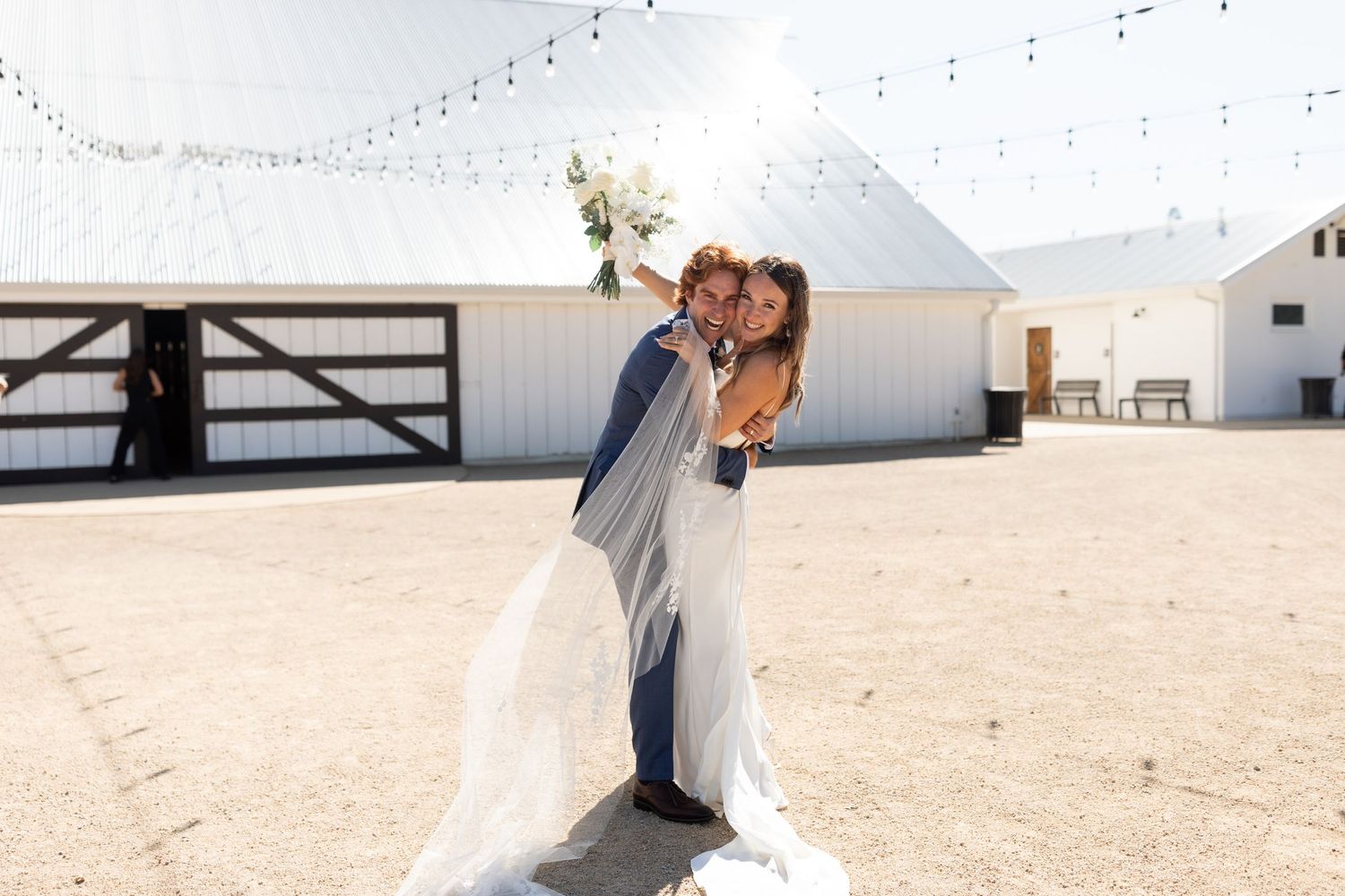 Newlyweds dancing under string lights at rustic outdoor venue.
