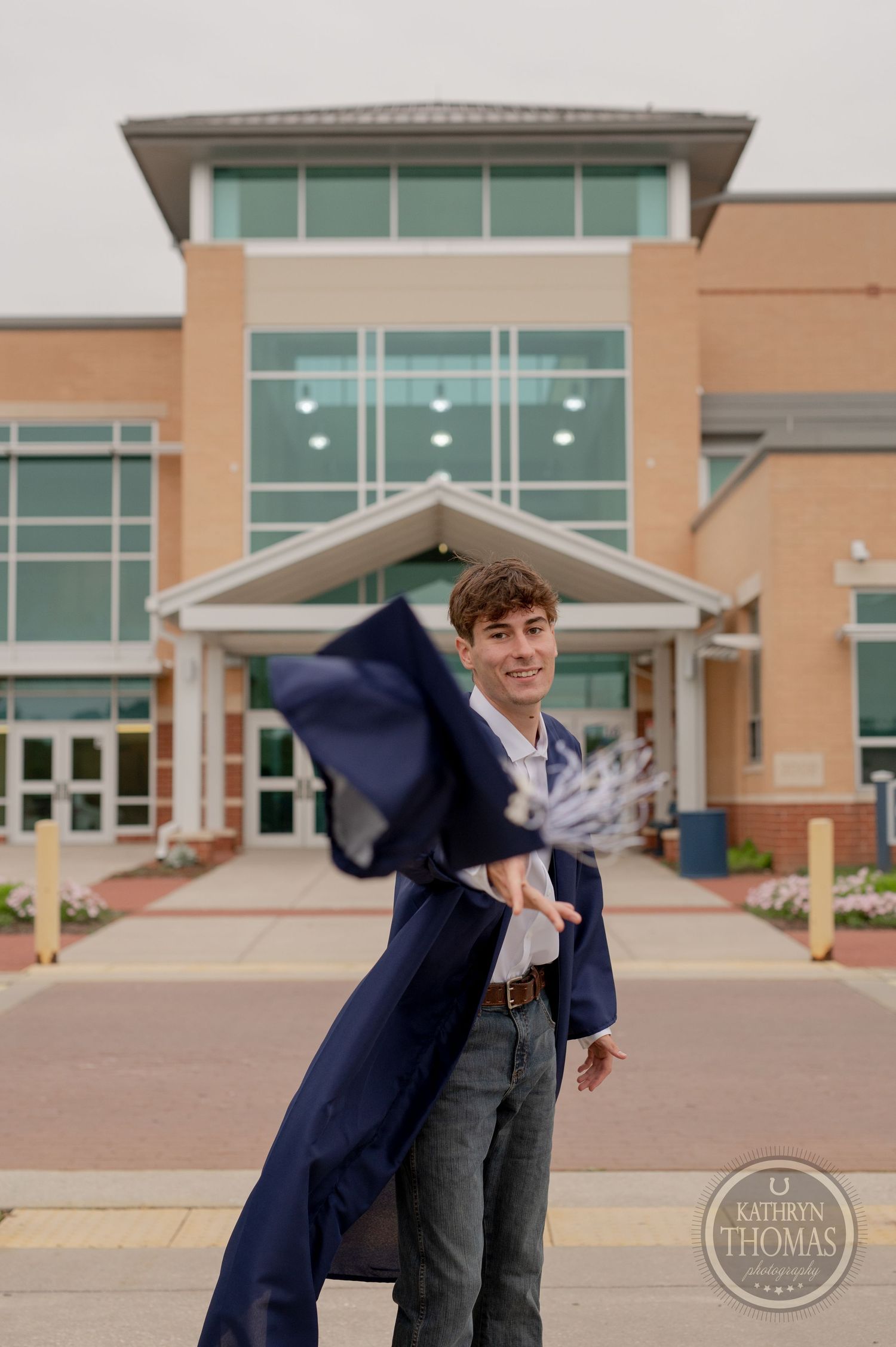 Navy graduation gown swirls in wind outside modern educational facility entrance.