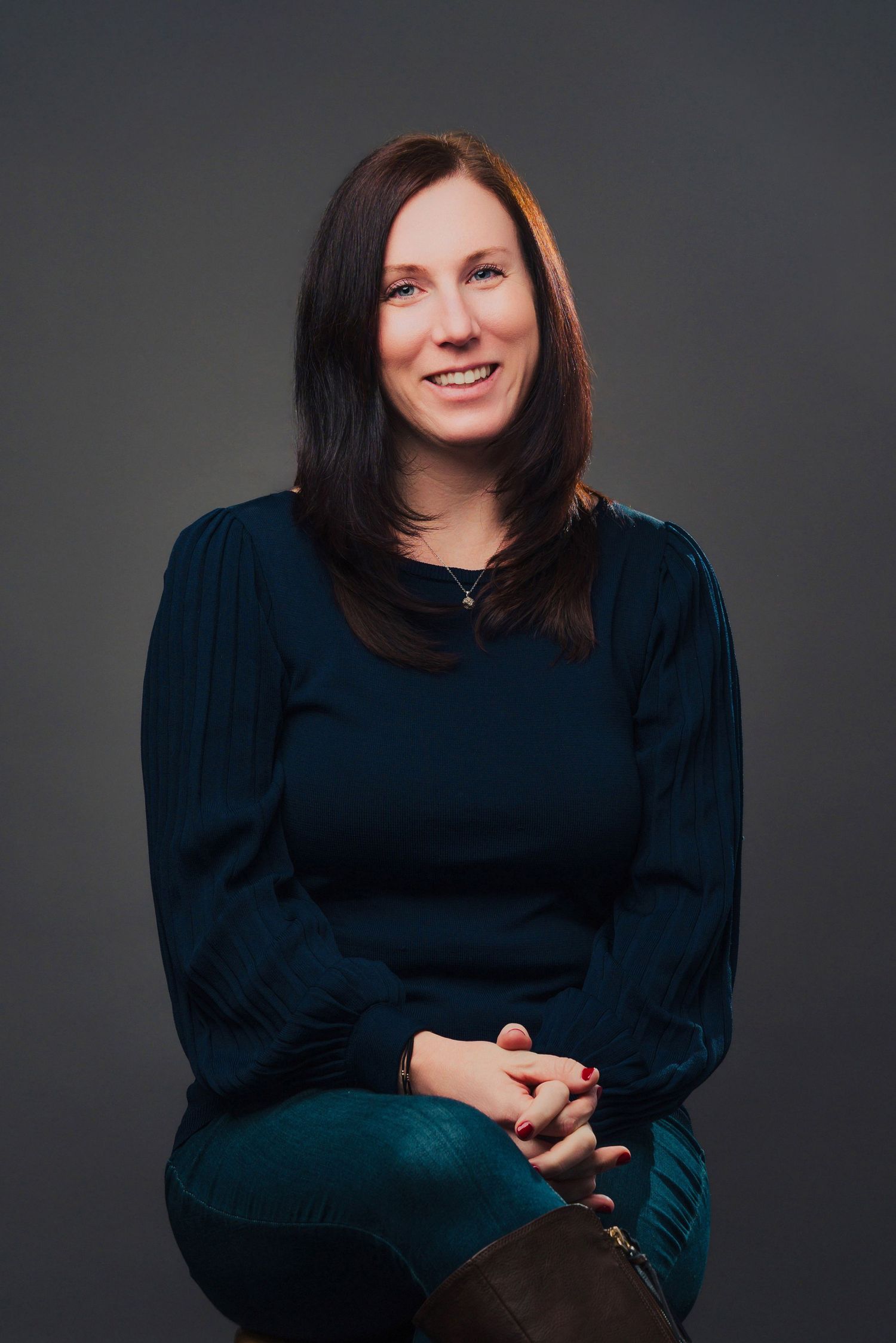 Professional headshot of person wearing maroon blazer and white blouse against neutral background.