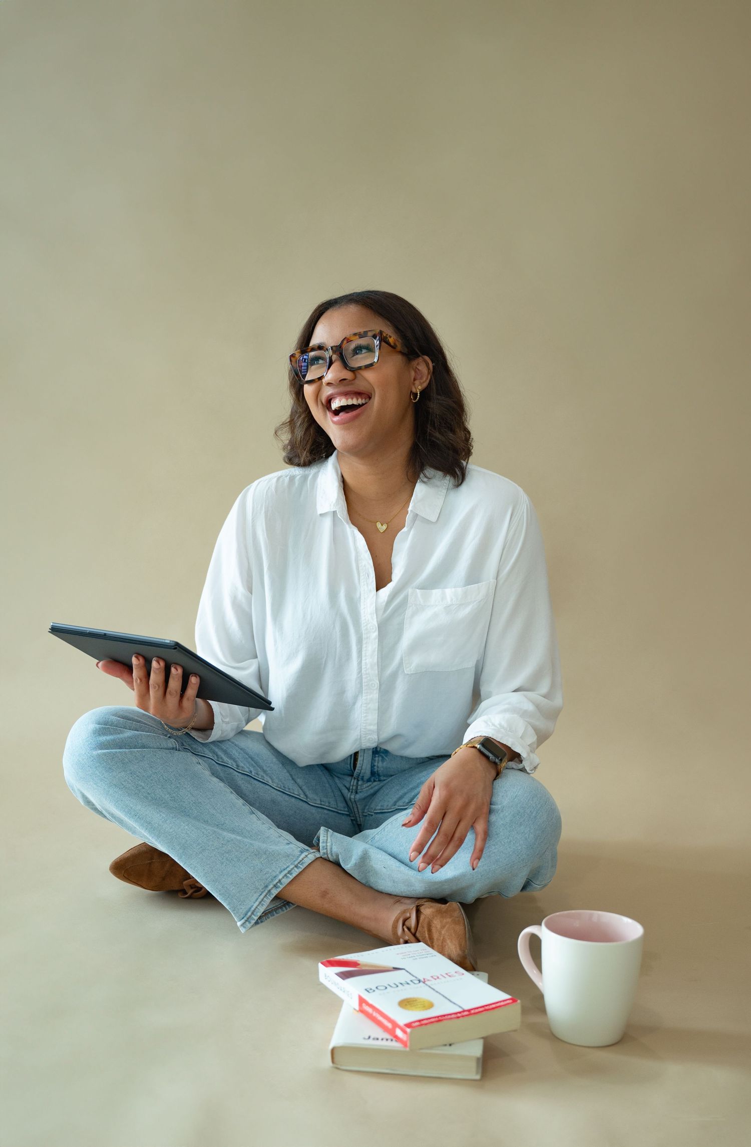 Person sitting cross-legged with tablet and coffee while working in casual home office setting.