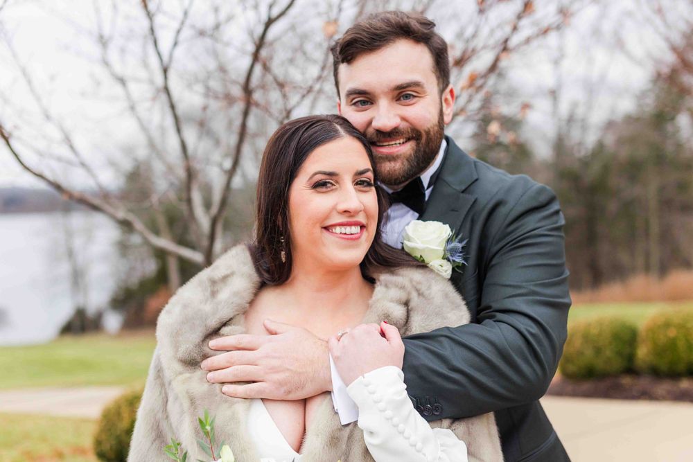 A happy couple embraces outdoors on their wedding day, wearing formal attire with a natural winter landscape behind them.