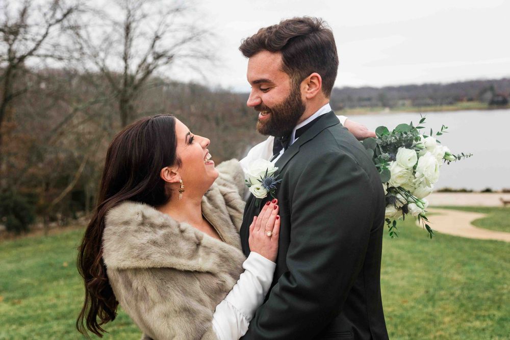 A couple shares a romantic moment outdoors in autumn wearing elegant wedding attire with a bouquet of white flowers.