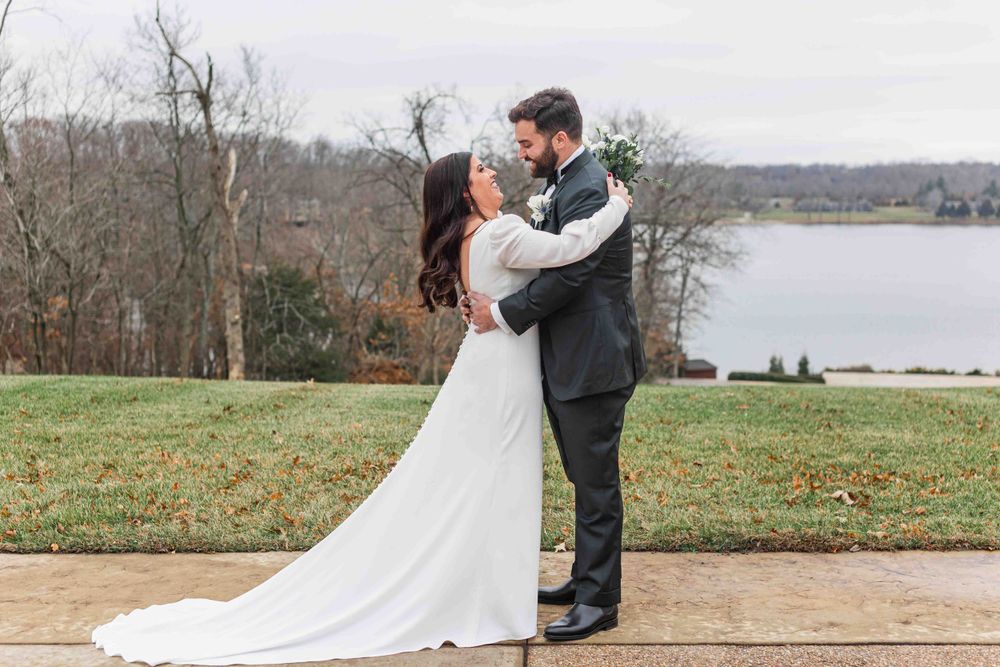 A couple embraces during their outdoor wedding ceremony overlooking a serene lake on a cloudy winter day.