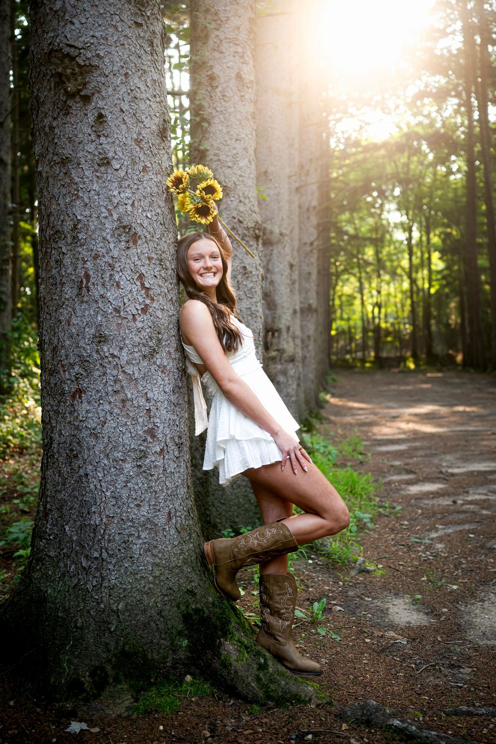 Sunlit forest photography session with a rustic tree trunk backdrop and cowboy boots.