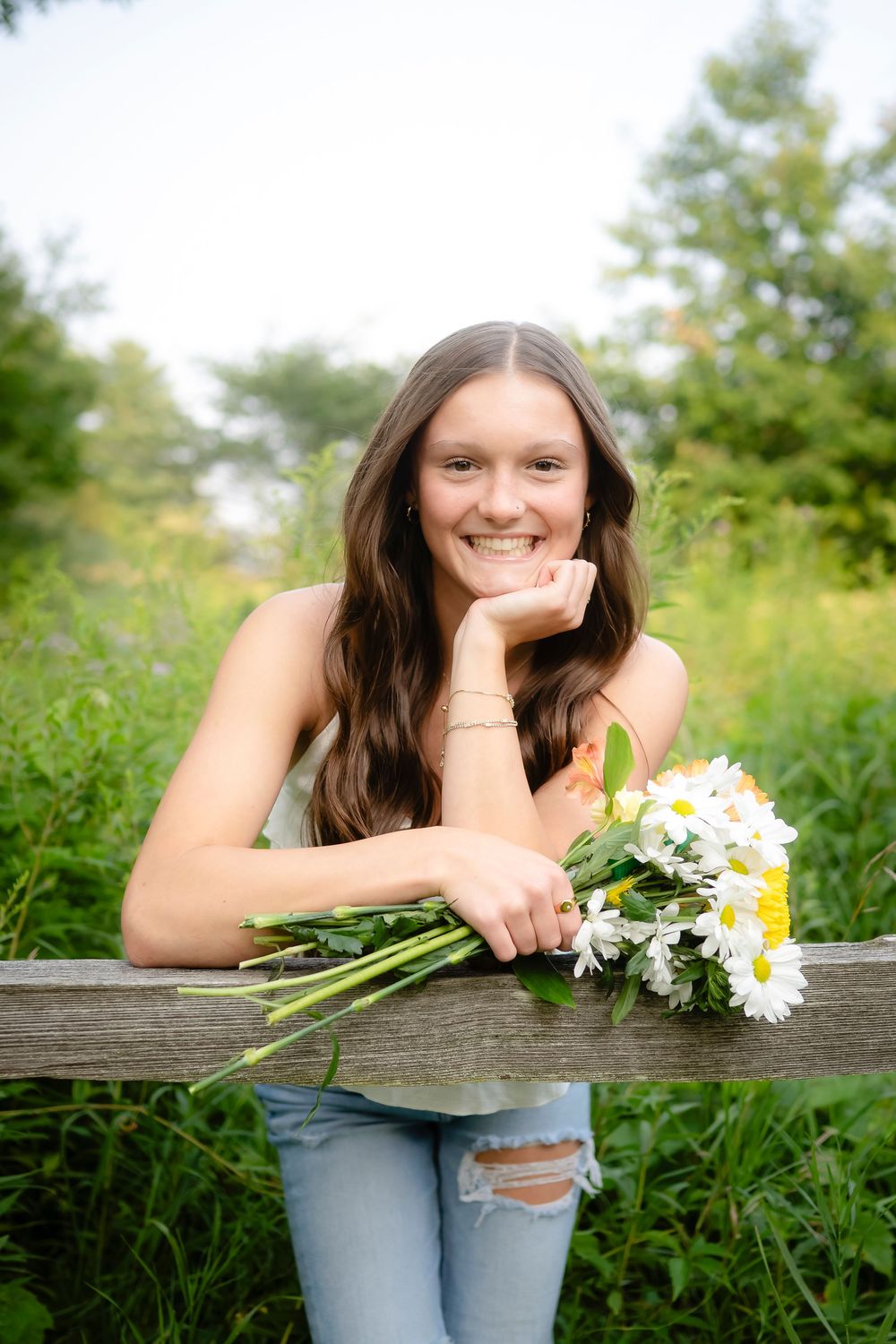 Casual portrait with daisies on a wooden fence in a natural outdoor setting.